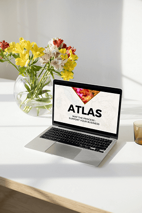 This is an image of the ATLAS Workshop shown on a laptop screen on a white desk with a vase of yellow, white and red flowers.